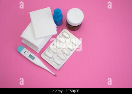 Gewebe, Nasentropfen, Thermometer, Pillen und Blister auf rosa Hintergrund. Stockfoto