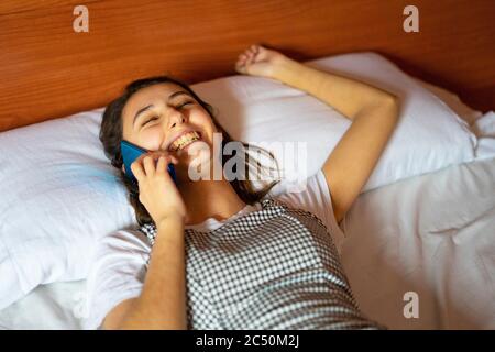 Frau liegt im Bett und spricht am Telefon. Lachend auf einen Anruf. Mit der Familie am Telefon sprechen. Stockfoto