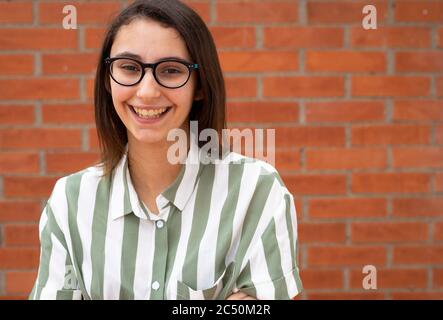 Geschäftsfrau in Brille und gestreiftem Hemd lächelt an einer Ziegelwand. Kopierbereich für Text. Stockfoto