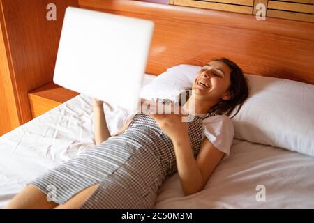 Frau lachend und mit Laptop im Bett. Wiedergabe eines Videos auf dem Computer. Glück zu Hause. Stockfoto