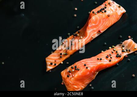 Roher Seerot Lachsfisch Filet zwei ungekochte Stücke mit bunten Pfefferkörnern auf schwarzem Hintergrund. Stockfoto