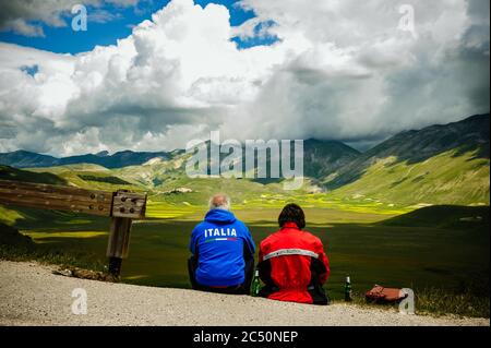 Castelluccio di Norcia, Umbrien, Italien - 21. Juni 2020: Das Biker-Paar bewundert das spektakuläre Panorama des Piano Grande in den Sibillini-Bergen. Stockfoto