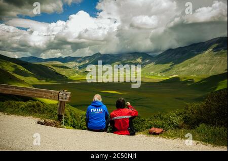 Castelluccio di Norcia, Umbrien, Italien - 21. Juni 2020: Das Biker-Paar bewundert das spektakuläre Panorama des Piano Grande in den Sibillini-Bergen. Stockfoto