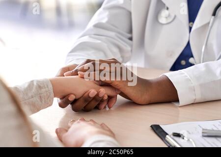 Afrikanischer Arzt hält Hand des kaukasischen Patienten geben Trost, Mitgefühl, Nahaufnahme. Stockfoto