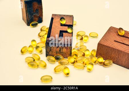Vitamin E weiche Gel Kapseln und Holz typografische Buchstaben E. Gesundheitswesen und Immunität Unterstützung Konzept. Stockfoto