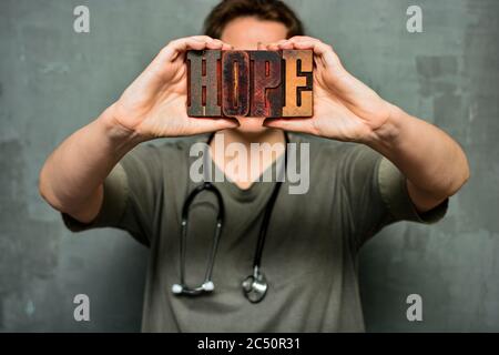 Ein Arzt mit Stethoskop hält das Wort "Hoffnung" aus hölzernen typografischen Buchstaben. Gesundheitspersonal, Krankenschwester, hochwertige medizinische Versorgung Stockfoto