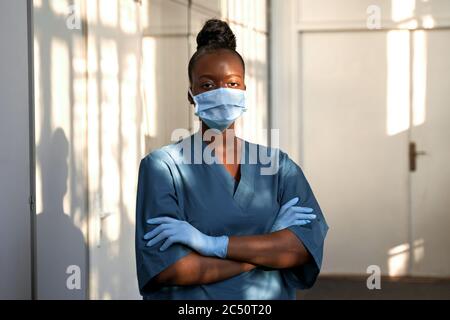 Zuversichtlich afrikanische Krankenschwester tragen blaue Uniform, Gesichtsmaske, im Krankenhaus stehen. Stockfoto