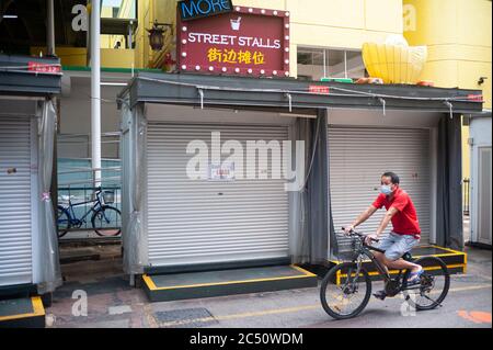 25.06.2020, Singapur, Republik Singapur, Asien - EIN Radfahrer trägt eine Schutzmaske und fährt an geschlossenen Straßenständen in Chinatown vorbei. Stockfoto