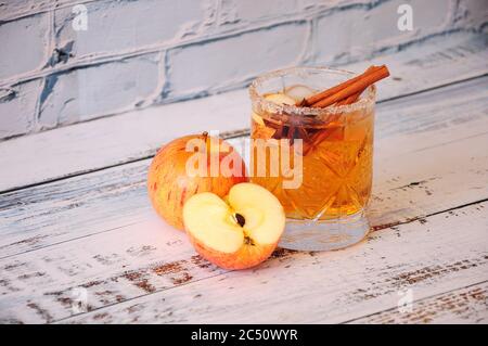 Ganze und geschnittene reife Äpfel stehen auf einem Tisch neben einem Kristallglas mit Anis und Zimtstangen. Nahaufnahme. Stockfoto