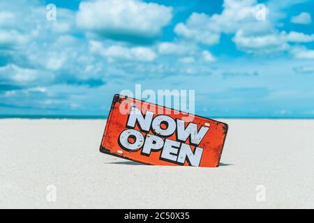 Jetzt offene Schild stehen auf Sand Sommer Strand Hintergrund Metapher zu Zeit zu reisen entspannen Tourismus Saison mit Copyspace Hintergrund. Stockfoto
