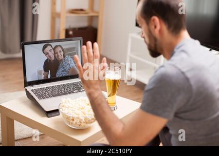 Mann winkt seinen Freunden in einem Videoanruf während der Quarantäne zu. Stockfoto