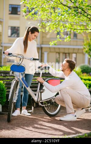 Frau, die Fahrrad unterstützt und Mann, der sich hinunterhockend Stockfoto