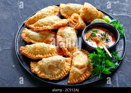 Hot Juicy Buffalo Chicken Empanadas mit kalorienarmer Dip auf einer schwarzen Platte auf einem Betontisch, horizontale Ansicht von oben Stockfoto