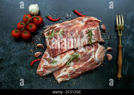 Racks roher Schweinefleisch-Spare-Rippen, gewürzt auf einer schwarzen Oberfläche Stockfoto