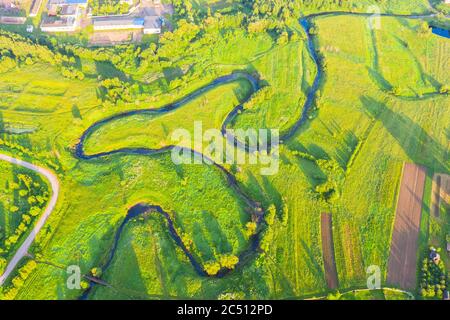 Top Luftaufnahme der natürlichen ländlichen Landschaft Tal eines gewundenen Flusses zwischen grünen Feldern und Wäldern Stockfoto