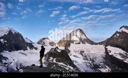 Zinal, Schweiz - 19. Juli 2019: Eine Wanderfrau, die den fantastischen Blick auf schneebedeckte Berge unter einem schönen, wolkigen Morgenhimmel bewundert. Dame Bergsteigerin auf felsigen Hügel Stockfoto