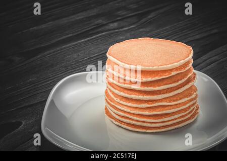 Ein Stapel frisch gebackener, hausgemachten duftenden Pfannkuchen auf einem weißen quadratischen Teller auf einem rustikalen Holztisch. Vorlage mit Platz für Kopieren und Platz für andere de Stockfoto