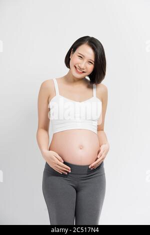 Schwangere Frau im Kleid hält die Hände auf dem Bauch auf einem weißen Hintergrund Stockfoto