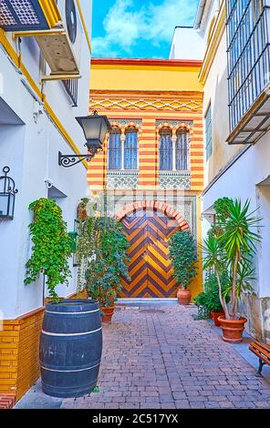 Der schattige Hof mit Pflanzen in Töpfen, alten Fass und Tor der historischen Mudejar Herrenhaus mit Zickzack-Muster, Sanlucar, Spanien Stockfoto