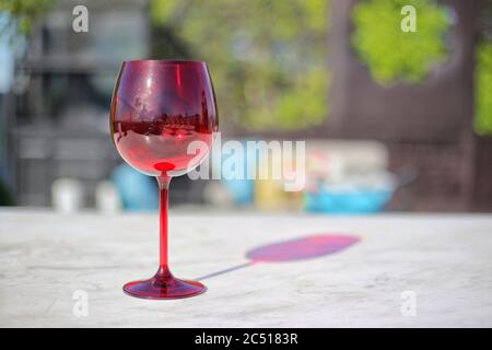 Rotwein Gläser Spirituosen Cocktails reflektieren blauen Himmel mit ein paar Wolken auf Marmortisch mit verwackelt bunten Sofa im Hintergrund. Stockfoto