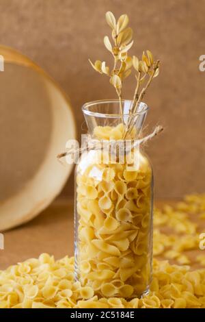 Pasta in einem Glas, ist eine Menge Pasta verstreut, ein Glas steht auf einem Holzständer Stockfoto