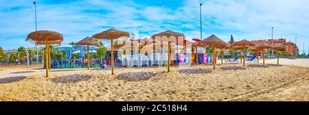 SANLUCAR, SPANIEN - 22. SEPTEMBER 2019: Die Sandbank von Calzada Strand mit Linie von Strohschirmen, Strandcafé und Wohnhäuser auf dem Hintergro Stockfoto