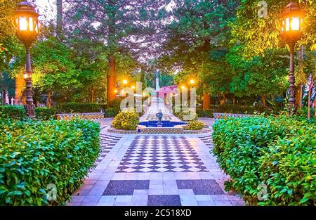 Abend im topiary Alameda Apodaca und Marques de Comillas Garten mit Schachbrettmuster Boden, ausgebreiteten Bäumen, getrimmten Büschen, Gusseisen Retro Laterne Stockfoto