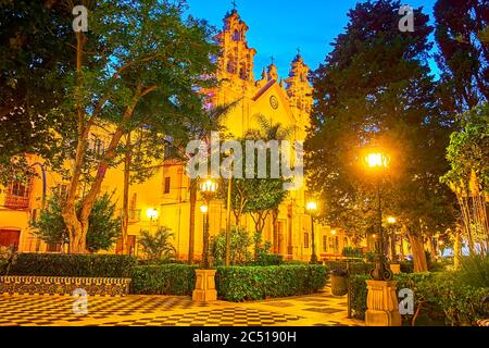 Die Carmen Kirche in hellen Stadtlichtern ist durch das üppige Grün des Alameda Apodaca Garten, Cadiz, Spanien gesehen Stockfoto