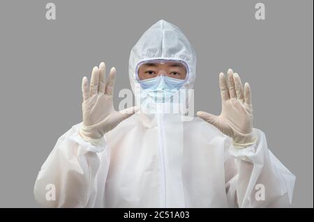 Ein asiatischer Mann, der Schutzanzug, medizinische Masken und eine Brille auf grauem Hintergrund trägt. Stockfoto