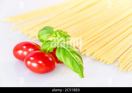 Ungekochte Pasta-Spaghetti, rote leckere Tomaten und grüne Basilikumblätter auf weißem Tisch Stockfoto