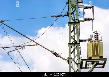 Grüner elektrischer Mast mit einem Transformator, der neben Eisenbahngleisen steht, dient zur Spannungsverteilung auf Eisenbahnlinien. Stockfoto