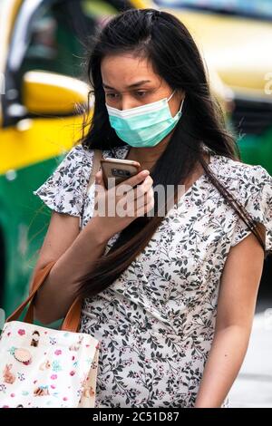 Mädchen trägt Gesichtsmaske mit Handy während covid 19 Pandemie, Bangkok, Thailand Stockfoto