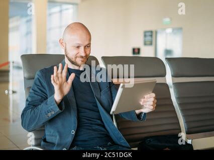Schöner kahlbärtiger lächelnder Mann Geschäftsmann im Anzug kommunizieren mit jemandem von Tablet in der Flughafenlounge Stockfoto