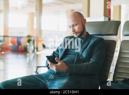 Ein gutaussehender Mann mit kahlem Bart, der in der Flughafenlounge ein Handy benutzte Stockfoto
