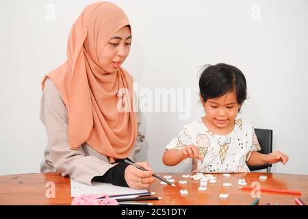 Muslimische Frau mit ihrem niedlichen Mädchen Tochter lernen und spielen zusammen zu Hause. Home School Bildung, Eltern lehren Kinder zu Hause. Frohe Familie. Mo Stockfoto