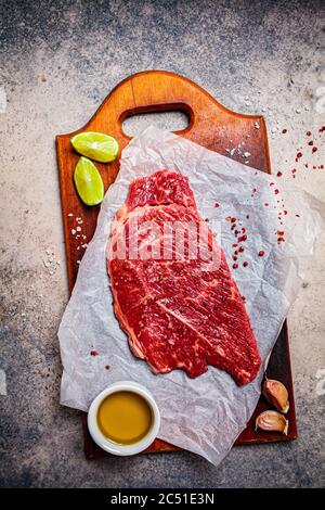 Rohes Rindfleisch mit Gewürzen auf Holzbrett, dunkler Hintergrund, Kopierraum. Stockfoto