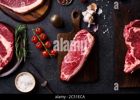 Draufsicht Sorte von frischen Black Angus Prime Roh Beef Steaks: Striploin, Chuck Roll und Picanha auf Cutiing Boards mit frischen chery Tomaten, Knoblauch und Stockfoto