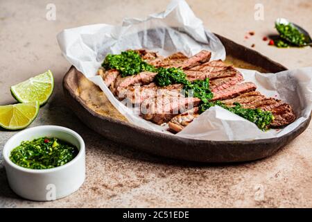 Rindersteak in Scheiben mit Chimichurri-Sauce auf dunklem, dunklem Hintergrund. Stockfoto