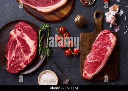 Draufsicht Sorte von frischen Black Angus Prime Roh Beef Steaks: Striploin, Chuck Roll und Picanha auf Cutiing Boards mit frischen chery Tomaten, Knoblauch und Stockfoto