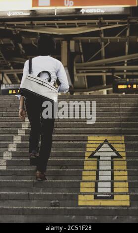 Ein Mann, der die Treppe zu einem Bahnsteig hinauf steigt, neben einem leuchtend weißen und gelben Pfeil, der auf den Stufen gemalt ist Stockfoto