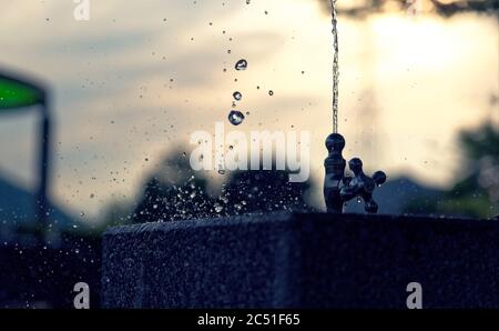 Wasser schießt aus einem Brunnen und spritzt auf dem Becken unten im späten Nachmittagslicht Stockfoto