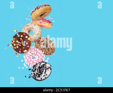 Fliegende glasierte runde Donuts. Mix aus bunten süßen Donuts mit Streuseln auf blauem Hintergrund Stockfoto