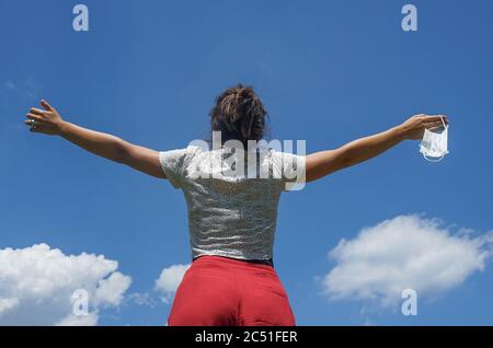 Frau mit den Armen ausgestreckt zum Himmel mit Schutzmaske in der Hand. Konzept des Endes der Coronavirus-Pandemie und Freiheit gefunden. Lebendige Farben. Stockfoto