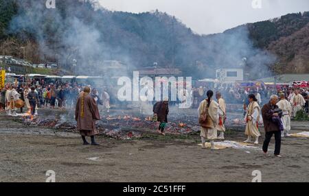 Eine alte Frau überquert den Feuerwanderplatz als Mönche und eine große Menschenmenge beobachten das jährliche Feuerwanderfest in der Nähe des Mount Takao, westlich von Tokio Stockfoto