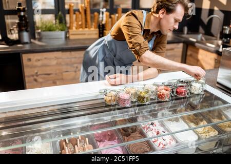 Konditor versucht verschiedene Lebensmittelzusatzstoffe in Form von Belag für Eis an der Theke eines Geschäfts Stockfoto