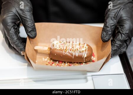 Schokoladeneis auf einem Stock mit verschiedenen Belägen auf einer Pappe, Nahaufnahme Stockfoto