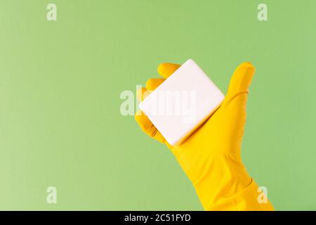 Hand in einem gelben Gummihandschuh mit Seife auf grünem Hintergrund Stockfoto
