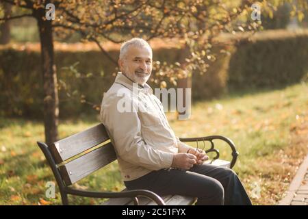 Alter grauhaariger Mann Rest auf der Bank im Herbst Park Stockfoto