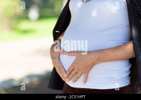 Herzförmige Hände auf dem Bauch einer schwangeren Frau, als Symbol der Liebe für das Kind, das geboren werden wird. Stockfoto