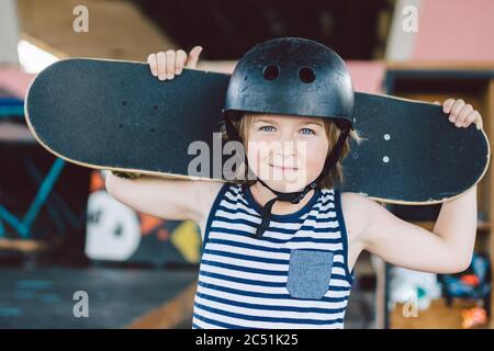 Skateboarder Junge in Helm posiert im Skate Park. Kid Boy mit Skateboard. Kindheit, Freizeit, Lifestyle-Konzept. Portrait stylish Junge Kind mit Skate Stockfoto